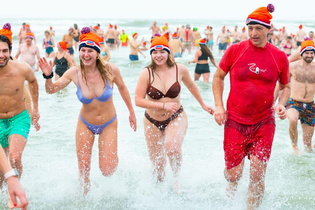 Twee meiden in Unox-muts rennen lachend uit de zee tijdens de Nieuwjaarsduik.
